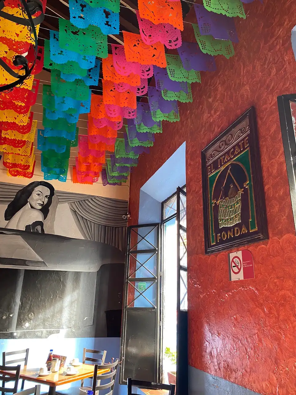Interior de El Itacate en Juan Soto: papel picado de colores, muro rojo y el mural de María Félix